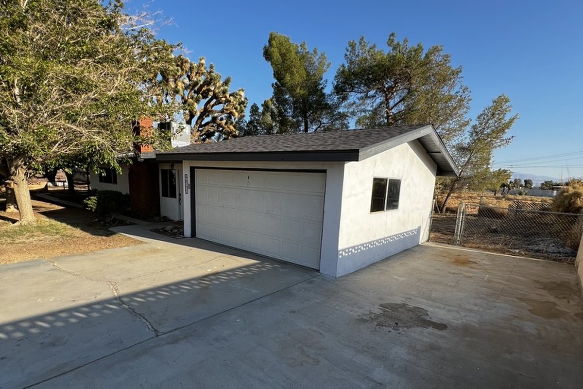 The same garage after renovation: repainted white with a new door and a newly poured concrete driveway
