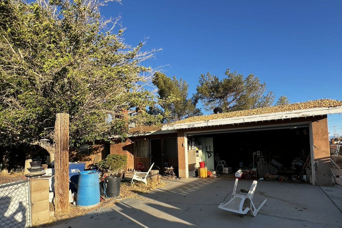 A garage and driveway before renovation: peeling paint, a cracked dirt driveway and stored junk